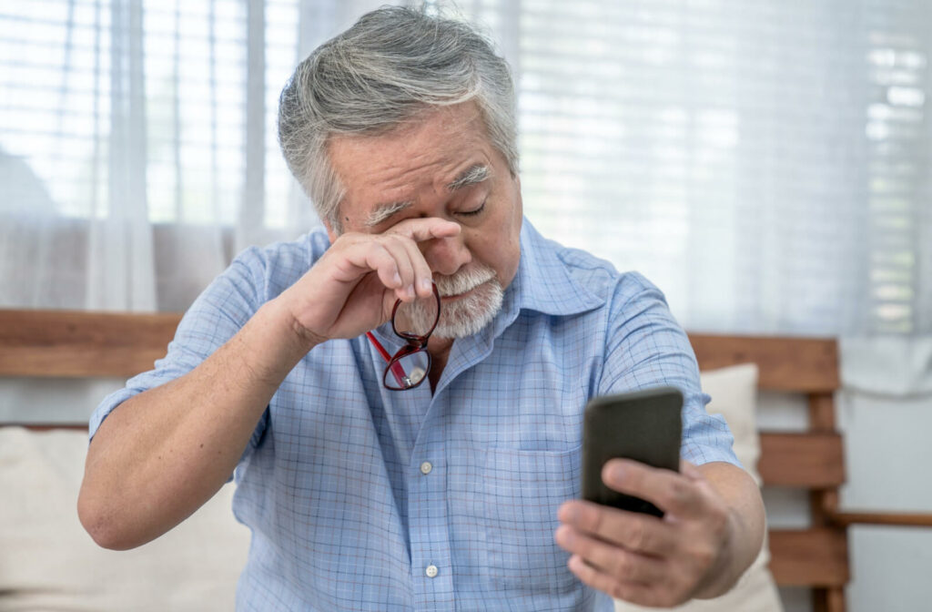 An elderly man is rubbing his right eye to get his vision clearer. Unable to read the messages on his phone.