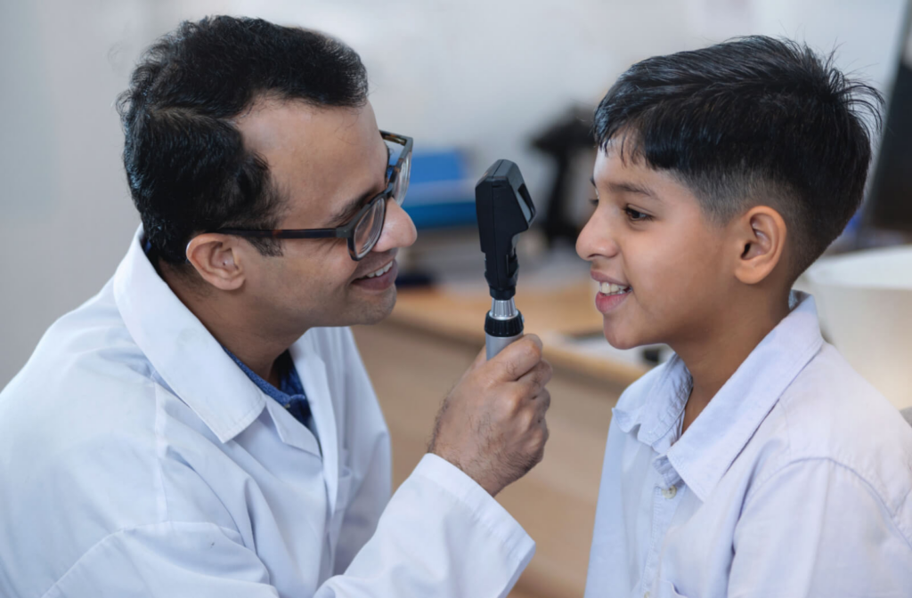 An optometrist conducts an eye exam on a young boy, both of them smiling.