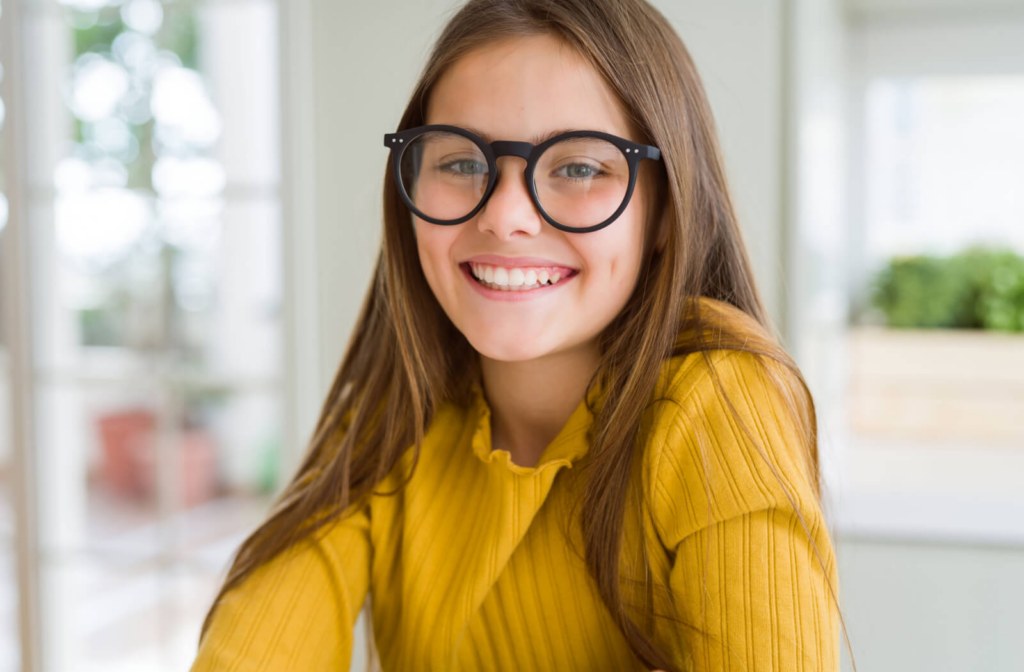 A young girl smiling, wearing eyeglasses and looking directly at the camera