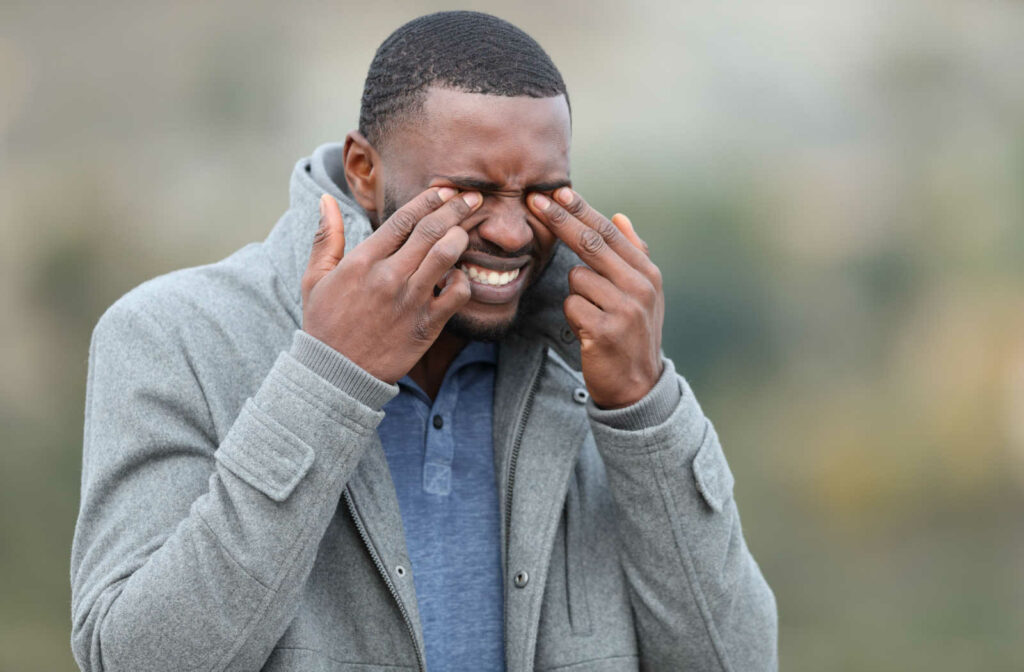 A young man in a jacket rubbing his eyes with both hands due to eye dryness.