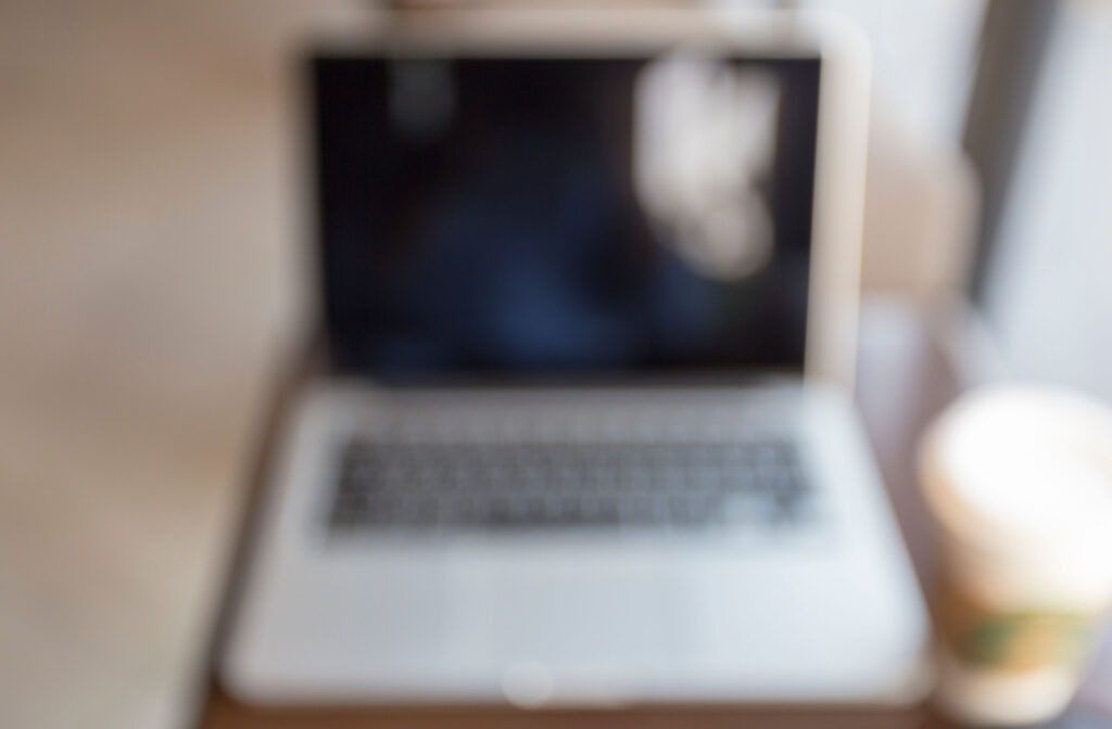 A POV of a person with blurry vision looking at their laptop and cup of coffee.