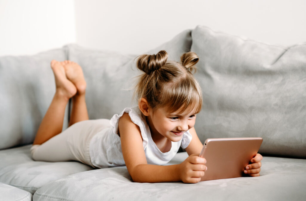 A young girl laying on the couch looking at an iPad screen.