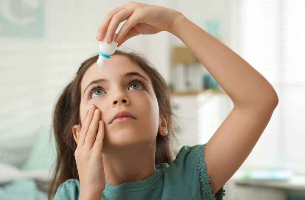 A young girl applying atropine eye drops on her right eye.