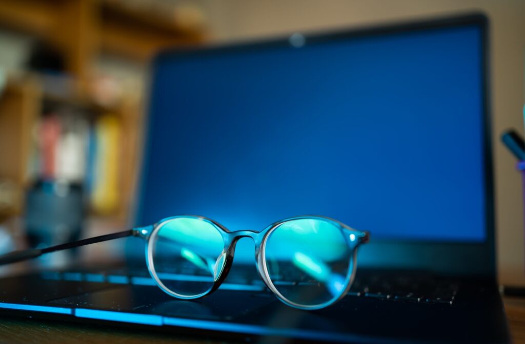 A pair of specialty glasses made to reduce eye strain, headaches, and dizziness sitting on an open laptop.