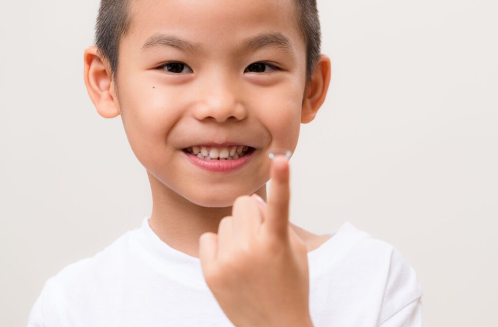 A young boy holding an overnight contact lens on his fingertip for myopia control.