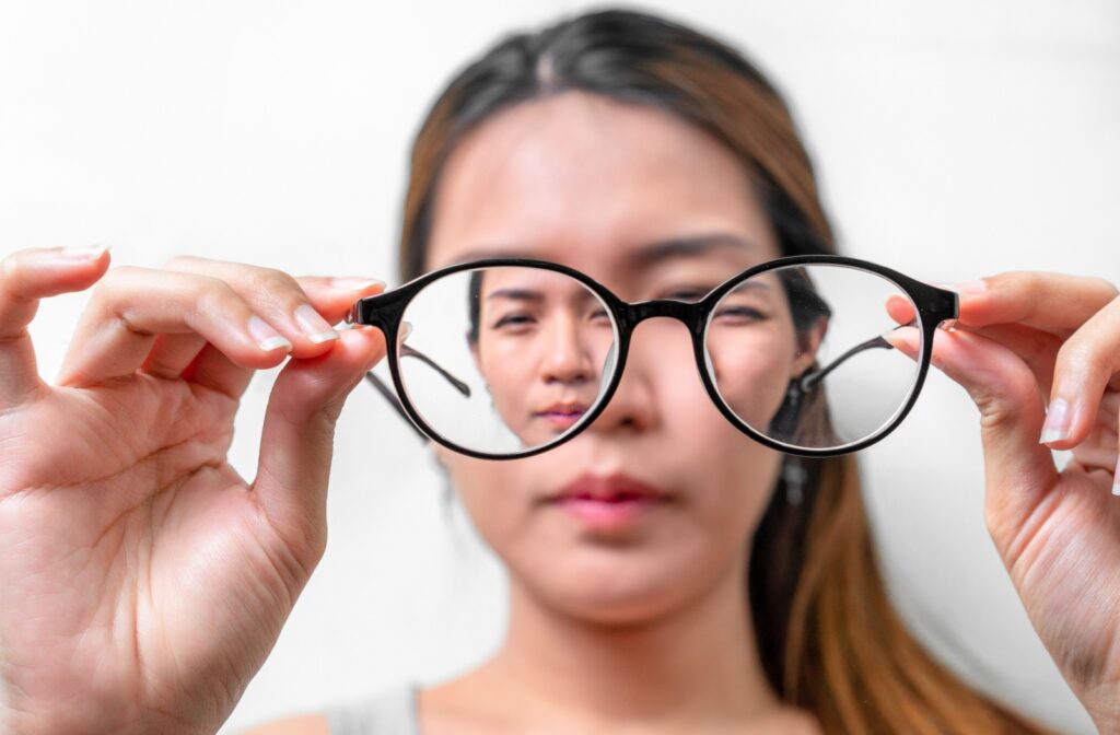 A woman holding out a pair of glasses in front of her face that help her see clearly due to myopia.