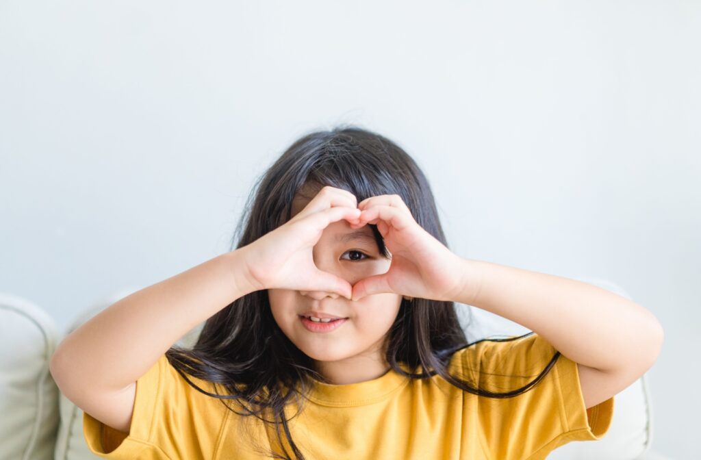 A young girl making a heart shape with her hands and holding it over her eye.