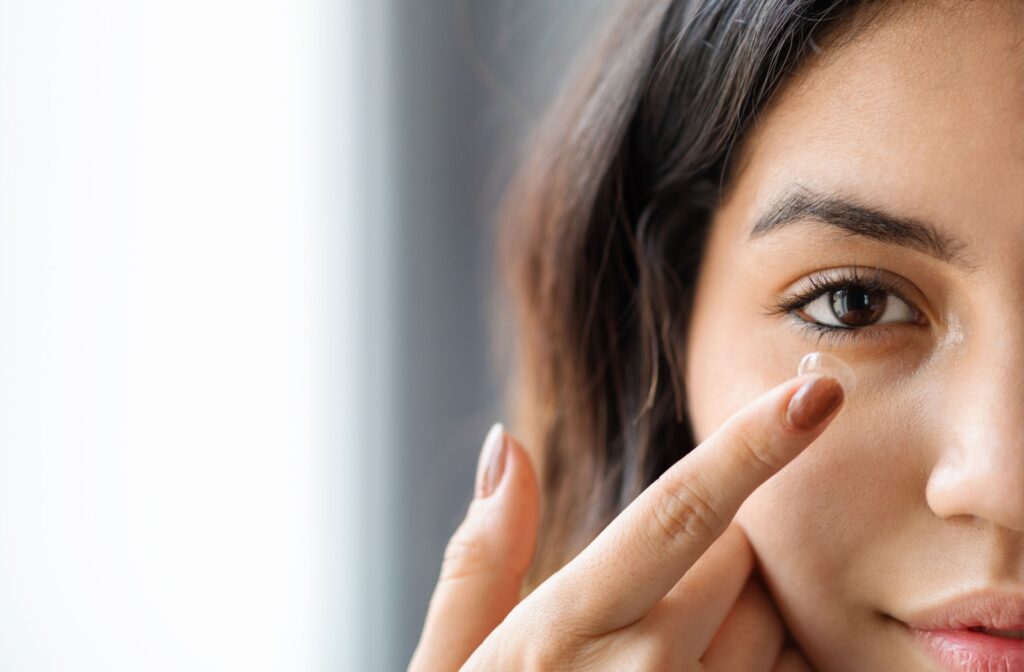 A female patient inserting a contact lens in her right eye using her right index finger.