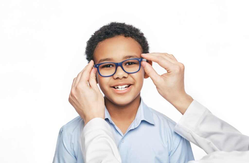 A smiling young boy being fitted for a pair of eyeglasses in front of a white background.