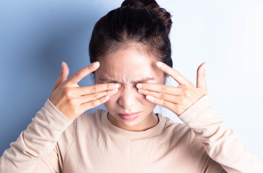 A close-up image of a woman squinting and rubbing her eyes due to dry eye discomfort.