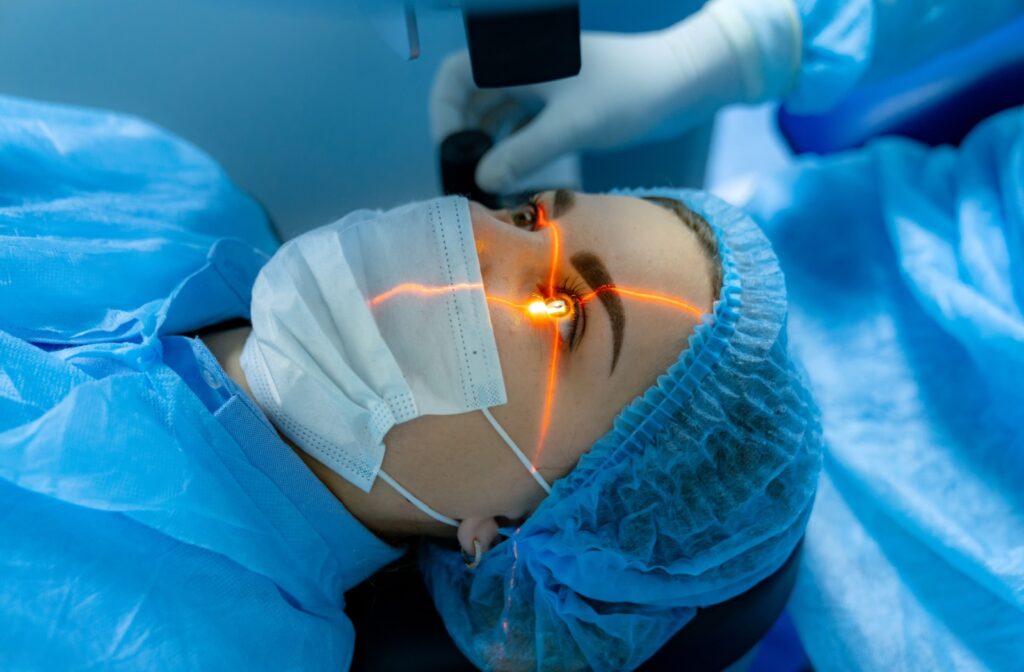 A woman in a mask lying down during laser eye surgery while the surgeon scans her left eye.