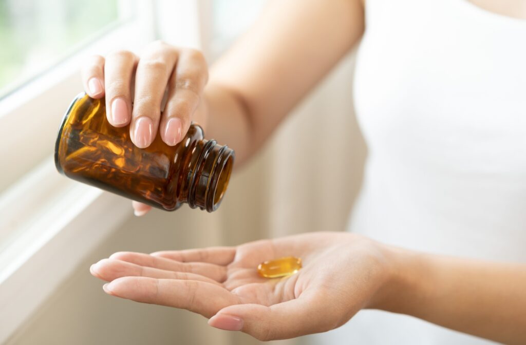 A person holding a brown bottle of vitamins and supplements for dry eye, dumping one capsule into their left hand.